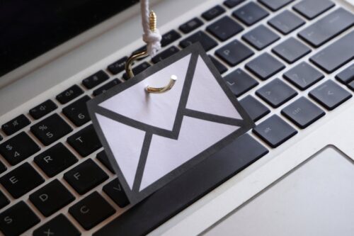 A hook holding an email logo hangs over a keyboard, representing the importance of phishing and cybersecurity training for employees